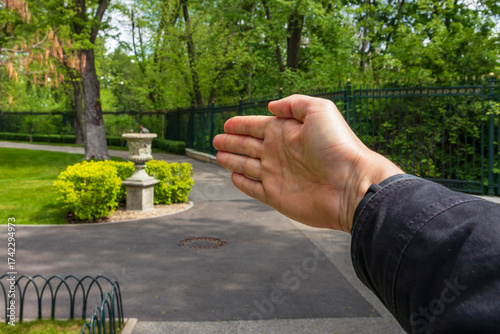 A man's hand pointing in a direction in a city garden or public park. A hint for a tourist or a guided tour