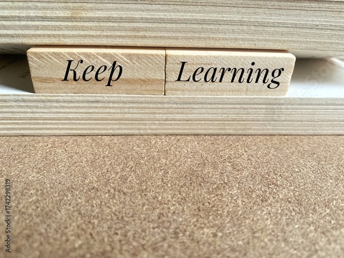 Two small wooden blocks placed between the pages of an open book, reading Keep Learning. Refers to the concept of lifelong learning or continuous self-improvement and education.