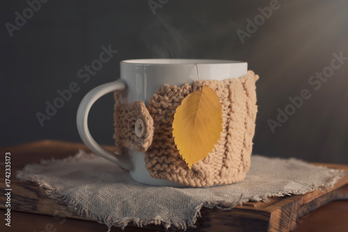 An autumn tea concept with a cozy cup in a knitted cover, steam, and a yellow leaf like a bag of brewing tea.