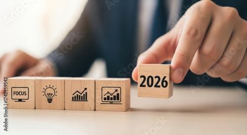 Businessman arranging wooden blocks with 2026, focus, idea, growth, and graph icons