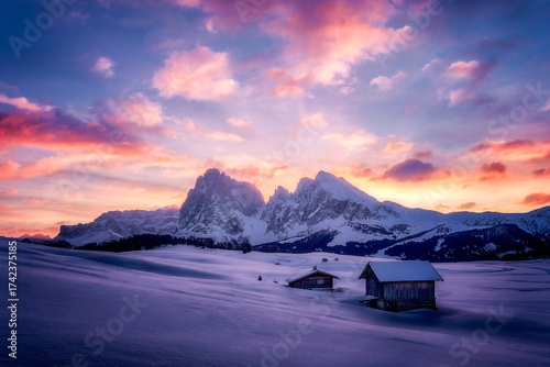 Snowy Mountain Sunset Over Alpe di Siusi With Cabins and Soft Pink Clouds A tranquil winter scene shows snow-covered fields and rustic cabins beneath towering alpine peaks as the sun sets, painting...