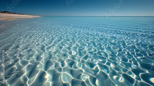 Pristine white beach meets crystal clear turquoise ocean, with dazzling sunlight on the shallow sandy seabed under a brilliant blue sky, creating a serene coastal panorama