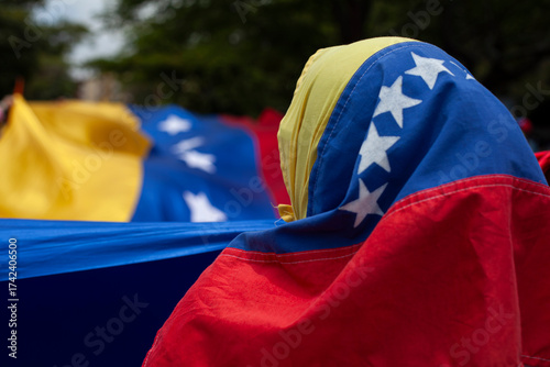Flags of Venezuela. An unrecognizable human figure wears a Venezuelan flag on his head.