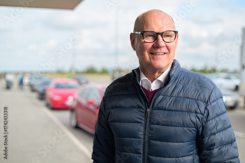 Happy senior Scandinavian man standing outdoors in front of a car park at an airport taxi area