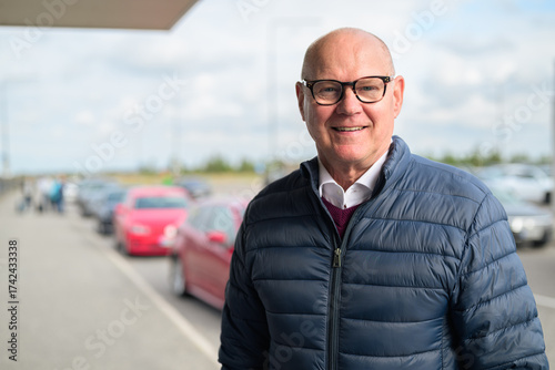 Happy senior Scandinavian man standing outdoors in front of a car park at an airport taxi area