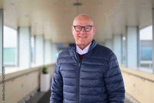 Portrait of a smiling senior Scandinavian man wearing eyeglasses in an airport corridor
