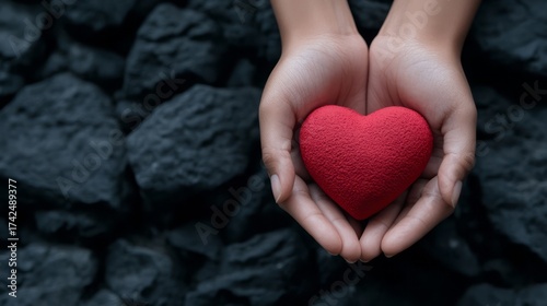 Hands Holding a Red Heart Against Dark Stone Background for Love and Care Concept
