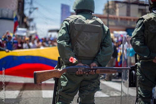 Photography A Venezuelan soldier from behind holds a rose, a symbol of violence and peace, next to his weapon