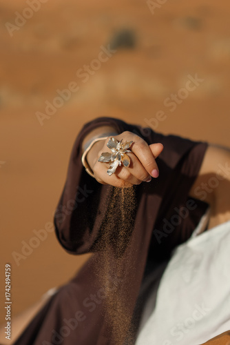 there's a beautiful ring on her hand, and yellow desert sand is falling