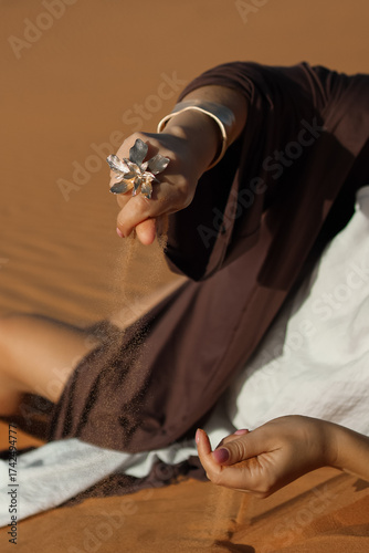 there's a beautiful ring on her hand, and yellow desert sand is falling