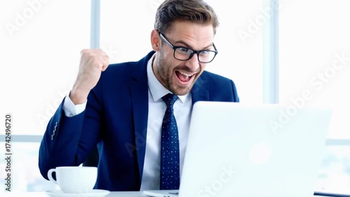 Excited businessman celebrates achievement looking at laptop, a dynamic scene showing success in a modern office setting with a coffee cup nearby