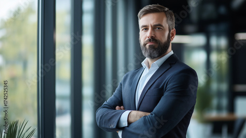 Confident bearded businessman looking out office window in sunlight
