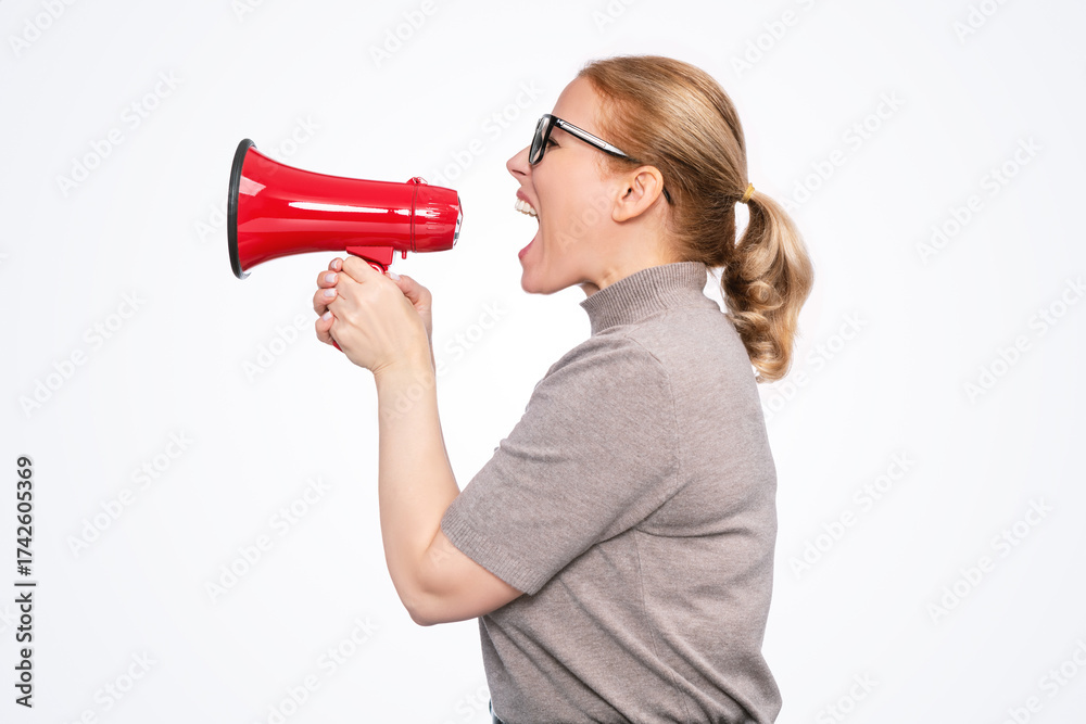Naklejka premium Side view of a woman shouting into a red megaphone, wearing glasses and casual clothes, isolated on light background. Concept of announcement, protest, sale, leadership, or communication.