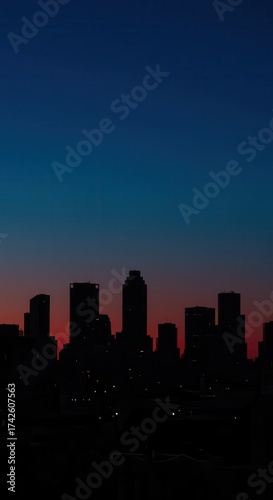The silhouette of a cityscape is defined against a gradient sky, showcasing a twilight atmosphere filled with blue and red hues as darkness descends.