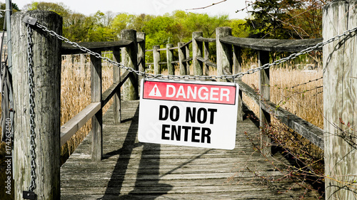 Sign warning of danger on wooden dock near marshland