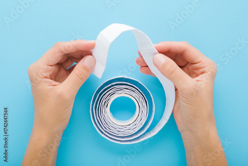 Young adult woman hands holding and showing new white double-sided stickers tape on light blue table background. Pastel color. Closeup. Point of view shot. Top down view.