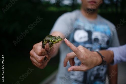 Man holding a frog by a creek with muddy hands
