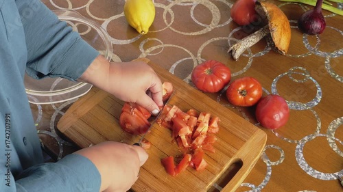 A woman's hand slices red home-grown tomatoes on a cutting board with a knife. Medium shot.