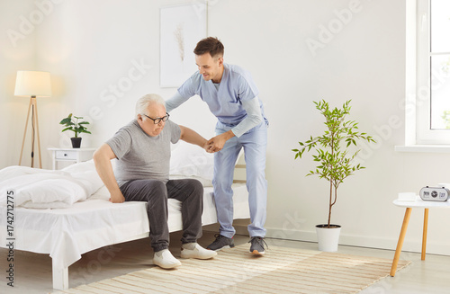 Fotografía Portrait of a young friendly male nurse helping a senior patient to get off the bed at home