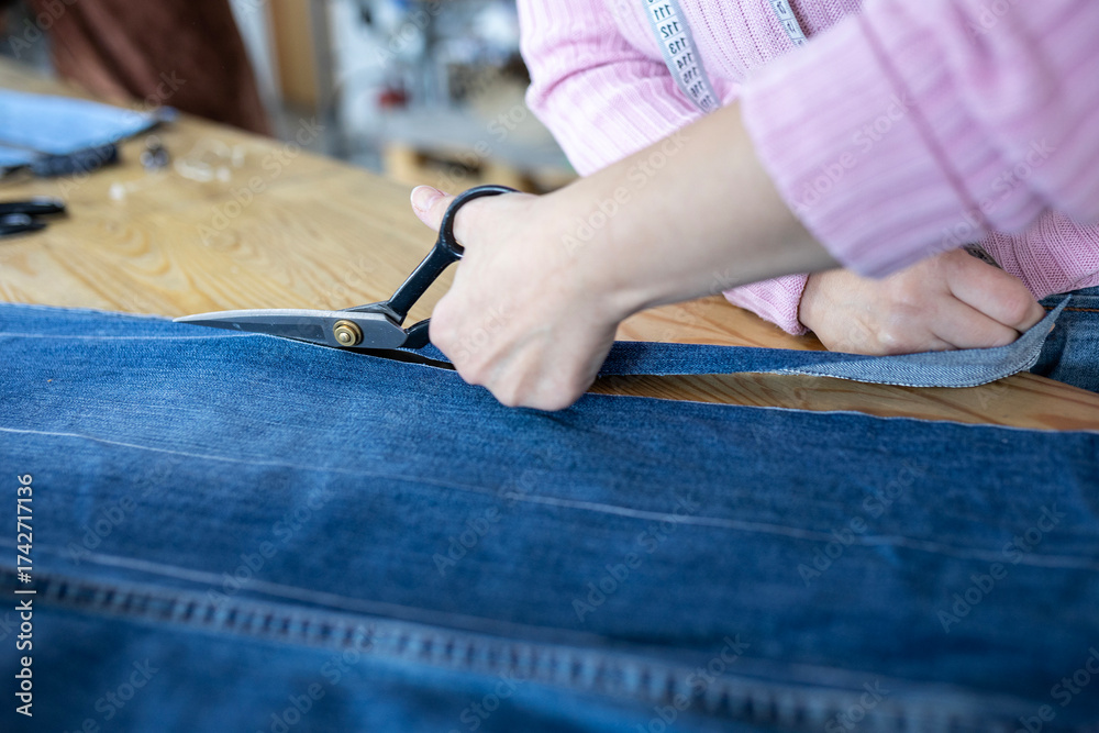 Obraz premium A designer cuts old jeans with tailor's shears to create a new garment. A concept of upcycling, recycling, and creating sustainable, eco-friendly fashion from denim.
