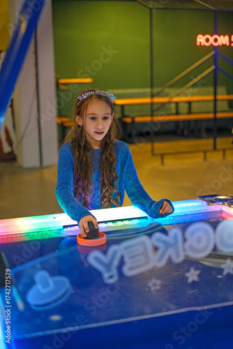 Focused on the game and competition, a girl plays table air hockey in an amusement park