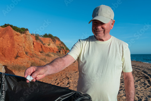 Hombre mayor tirando un papel a la basura en la  playa un día soleado con cielo azul.
