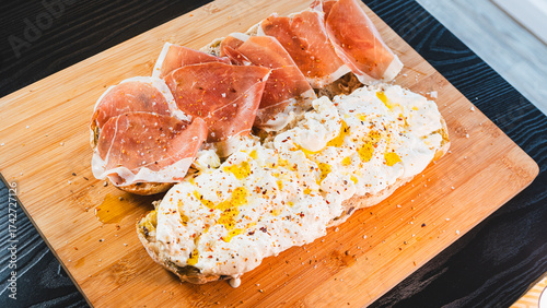 An open-faced sandwich showcasing creamy burrata cheese and delicate prosciutto on crispy ciabatta. Drizzled with olive oil and fresh herbs, this is pure Italian indulgence.