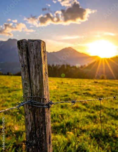 Golden sunset over mountainous terrain, fence post in foreground