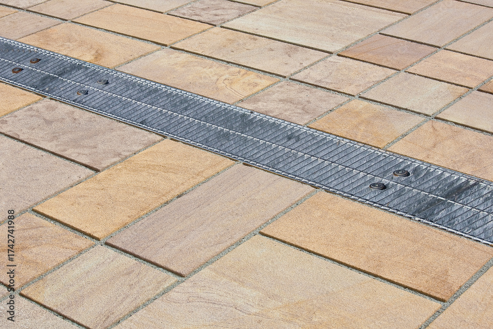 Fototapeta premium METAL RAINWATER COLLECTION GRID IN A PEDESTRIAN ZONE with concrete flooring made with blocks of rectangular shape