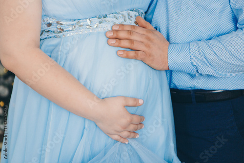 a man in a blue shirt hua man in a blue shirt hugs his wife's pregnant belly with his hand. girl in a blue dress. close up. High quality photo