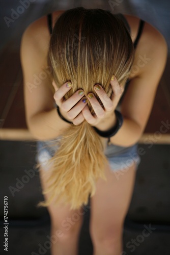 Woman with long blonde hair holding head in park 