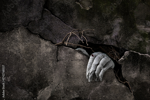 Mummy's hand wrapped in bandage rises through stone slabs of a grave or crypt. Background with copy space. Horrible risen dead mummy monster for Halloween horror concept