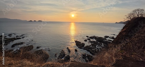 Golden sunset over rocky coastline, tranquil ocean viewin Costa Rica