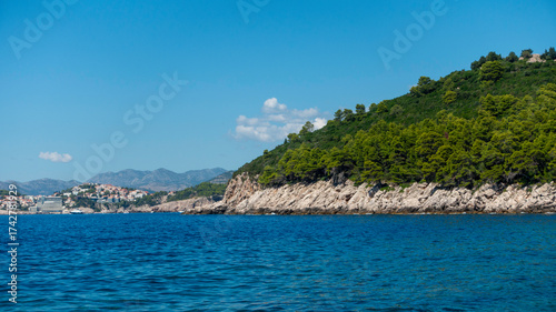 beautiful view on Lokrum island, rocky shore and green trees, calm sea and blue sky, ocean view for poster or wallpaper