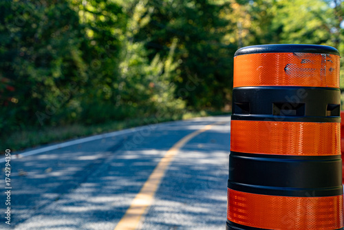Photography Close up of orange traffic barrel on a curved road.