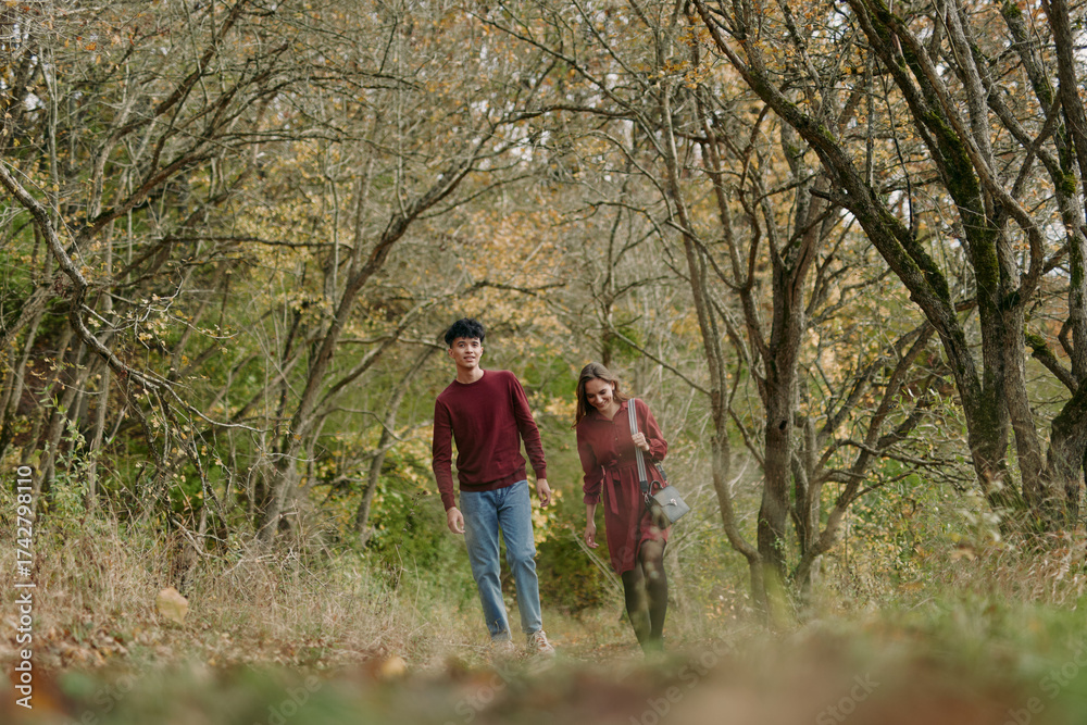 Obraz premium A candid outdoor portrait of a young couple walking through an autumn woodland path, natural expressions and relaxed posture conveying authentic connection and credible everyday intimacy.