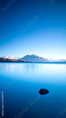 Serene, vast body of water reflecting mountains under a clear sky