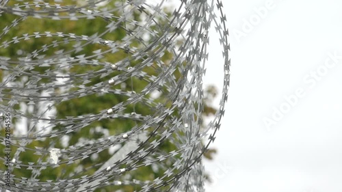 Razor wire and a tall security fence surround a white building with barred windows, indicating a high-security area such as a prison or detention center.