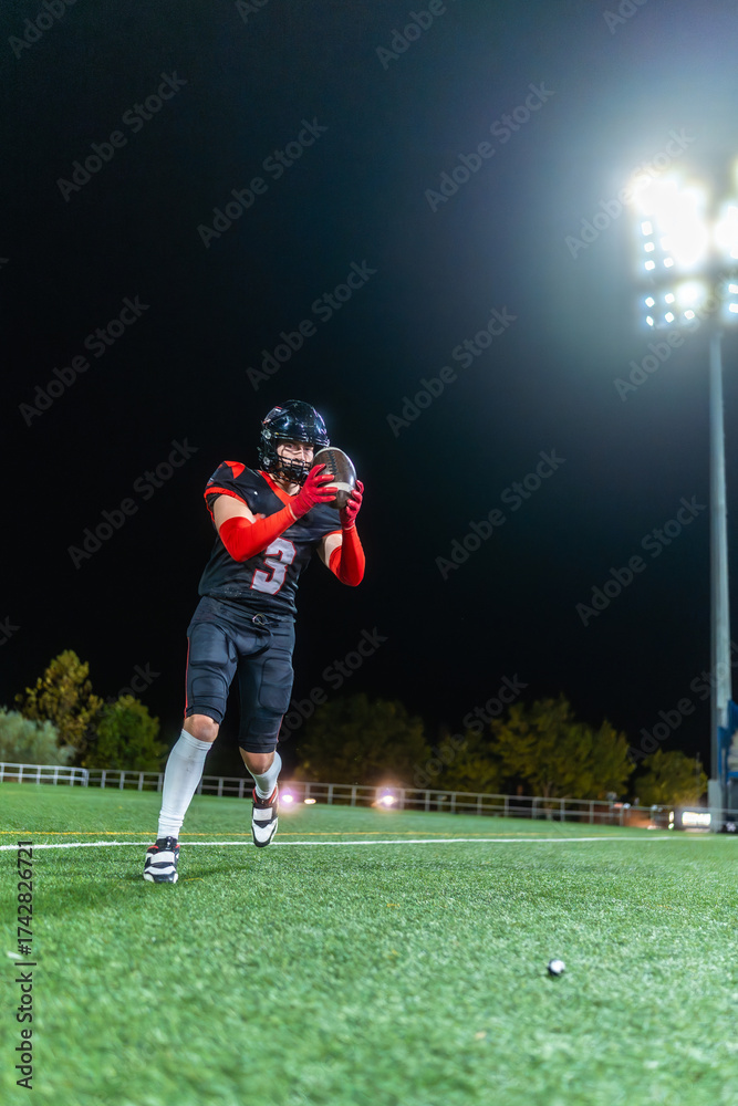 Naklejka premium American football player catching ball on field at night