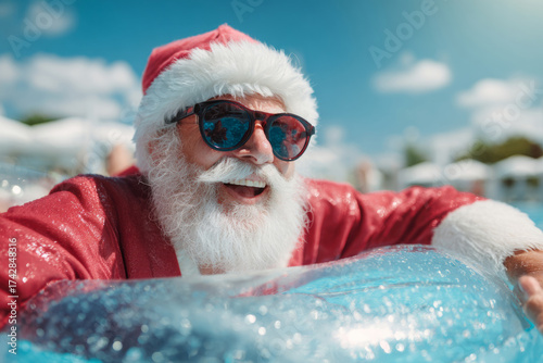 Santa Claus in red costume and hat wearing sunglasses floating on inflatable ring in pool