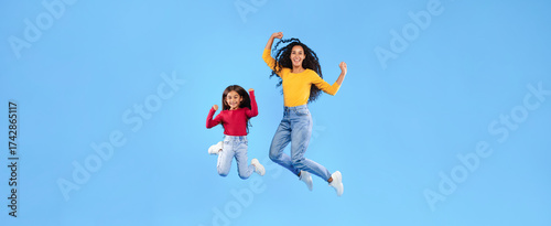Wallpaper Mural Happy Arabic Mother And Daughter Jumping Posing In Mid-Air Smiling To Camera Over Blue Background. Full Length Studio Shot Of Mom And Her Kid Celebrating Success Together And Having Fun Torontodigital.ca