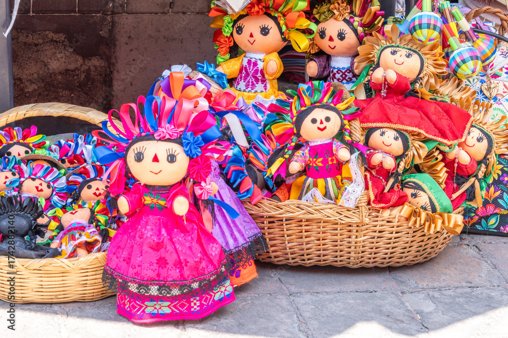 Fototapeta premium A collection of dolls with various outfits and accessories, including flowers and ribbons, are displ. Historic center of Queretaro, colonial architecture, decorations for the celebration of Mexico's I