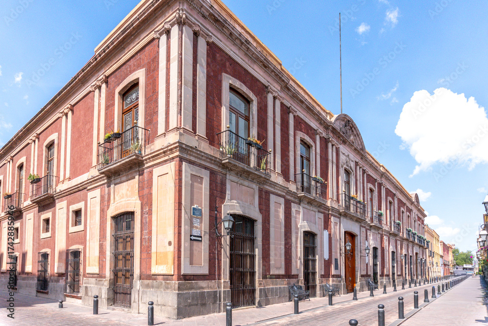 Fototapeta premium A large building with a red and white facade. The building has a lot of windows and balconies. Historic center of Queretaro, colonial architecture, decorations for the celebration of Mexico's Independ
