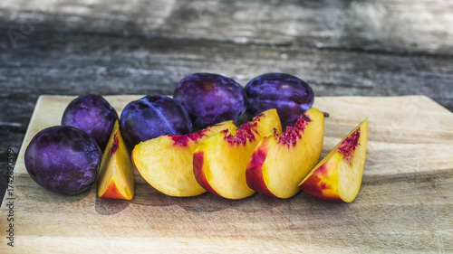 Freshly sliced peaches and plums arranged on a wooden cutting board in natural light