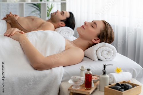 Caucasian couple customer enjoying relaxing anti-stress spa massage and pampering with beauty skin recreation leisure in day light ambient salon spa at luxury resort or hotel. Quiescent