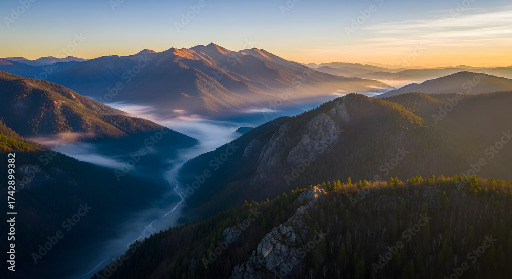 Fototapeta premium Majestic mountain range bathed in the warm glow of sunrise, with mist swirling through the valleys below