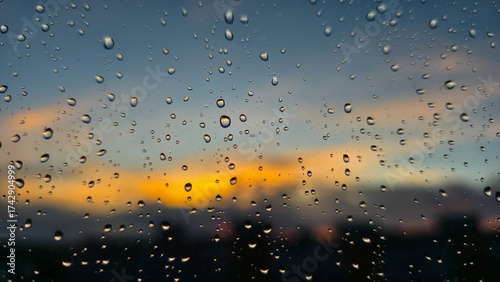 Close-up raindrops on window against glowing sunset sky. Warm light contrasts with cool tones, creating a tranquil and reflective mood of evening calm after gentle rain.