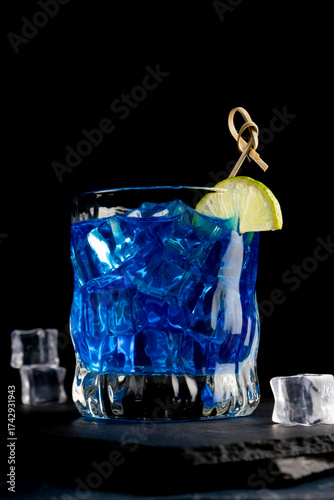 Colorful blue cocktail in a glass with a slice of lime on a black background