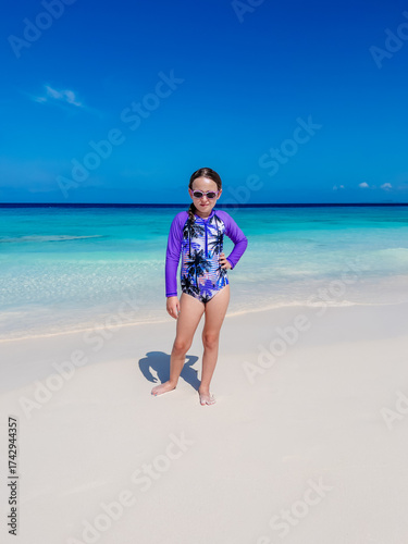 young girl in long sleeve one piece purple  swimsuit on a white sand beach in the Caribbean