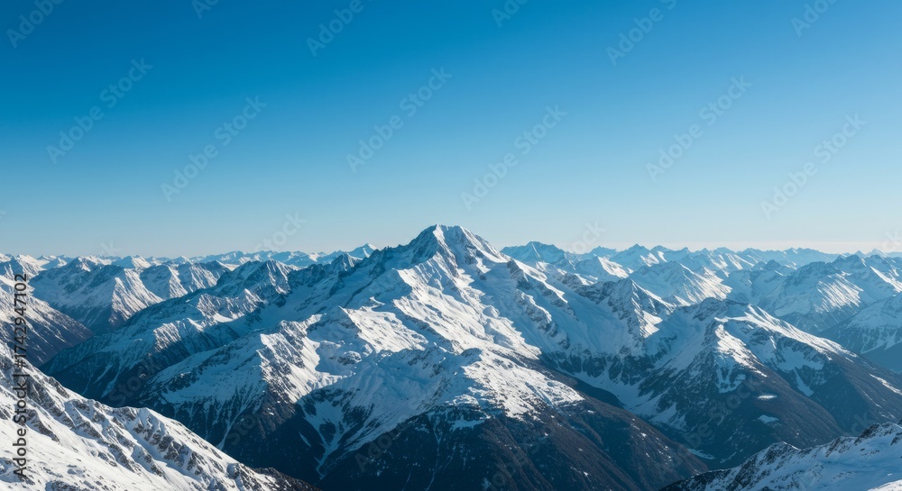 Obraz premium snow-covered mountain peaks under a clear blue sky, featuring a tall central summit surrounded by rugged slopes and deep valleys in a pristine winter landscape.
